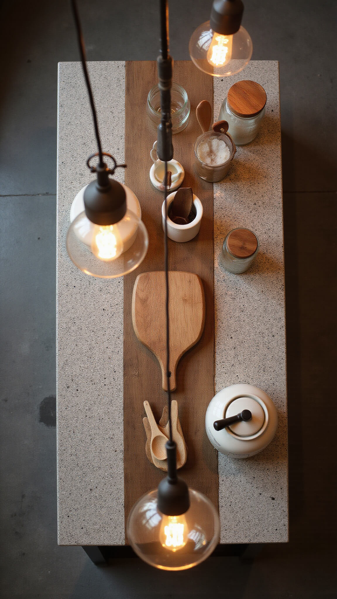 Overhead view of a 6ft kitchen island with honed granite top and reclaimed wood base, featuring cutting boards, ceramic crocks with utensils, and glass jars under warm pendant lighting at dusk.