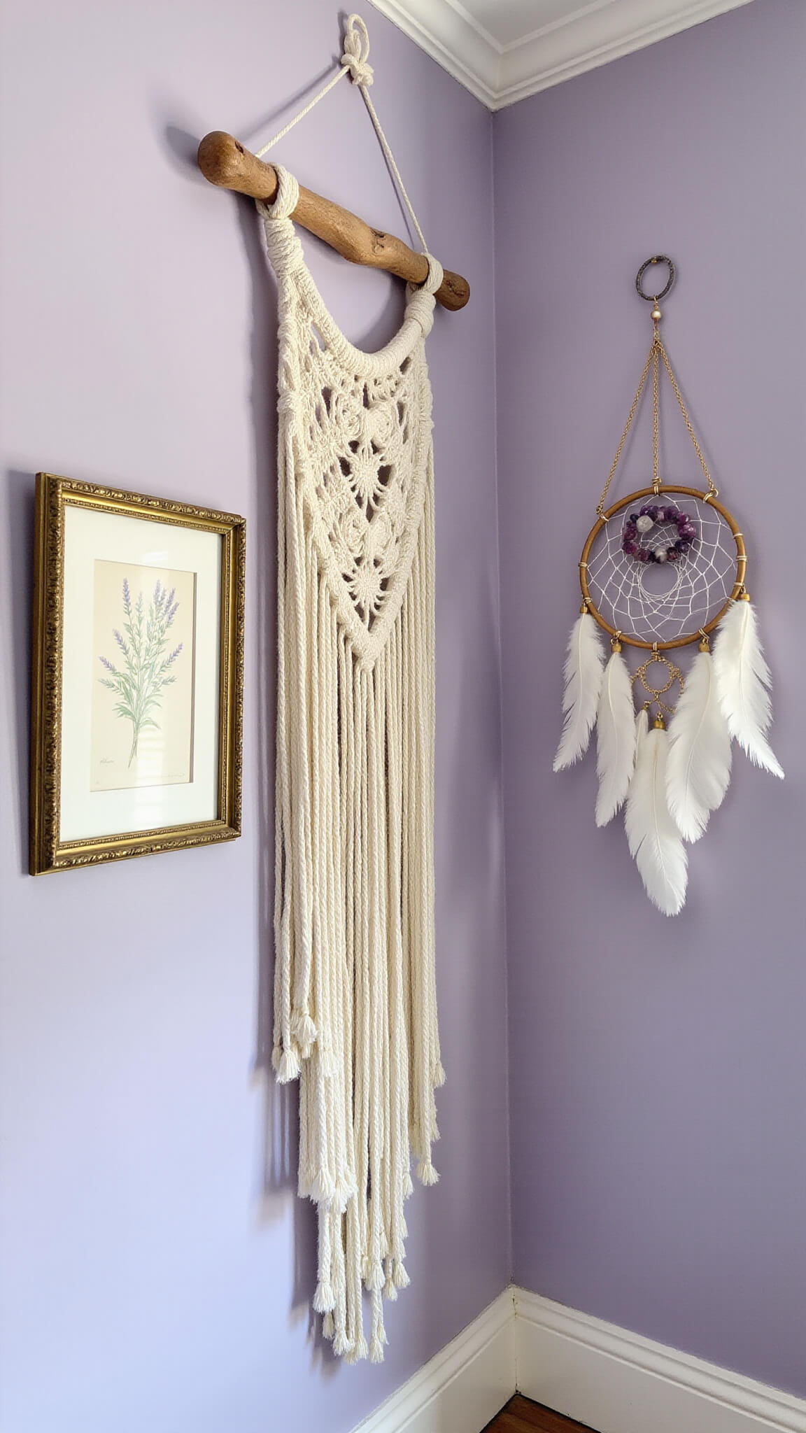 Corner view of a soft lavender accent wall with a large cotton macramé hanging, flanked by vintage gold-framed botanical prints and a dreamcatcher with purple agate beads and white feathers.