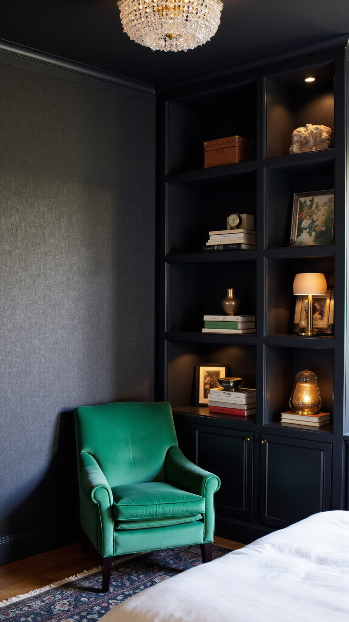Cozy black 11x13ft bedroom with vintage crystal chandelier, dark wallpaper, emerald velvet chair, black bookshelves, and layered lighting viewed from bed level.
