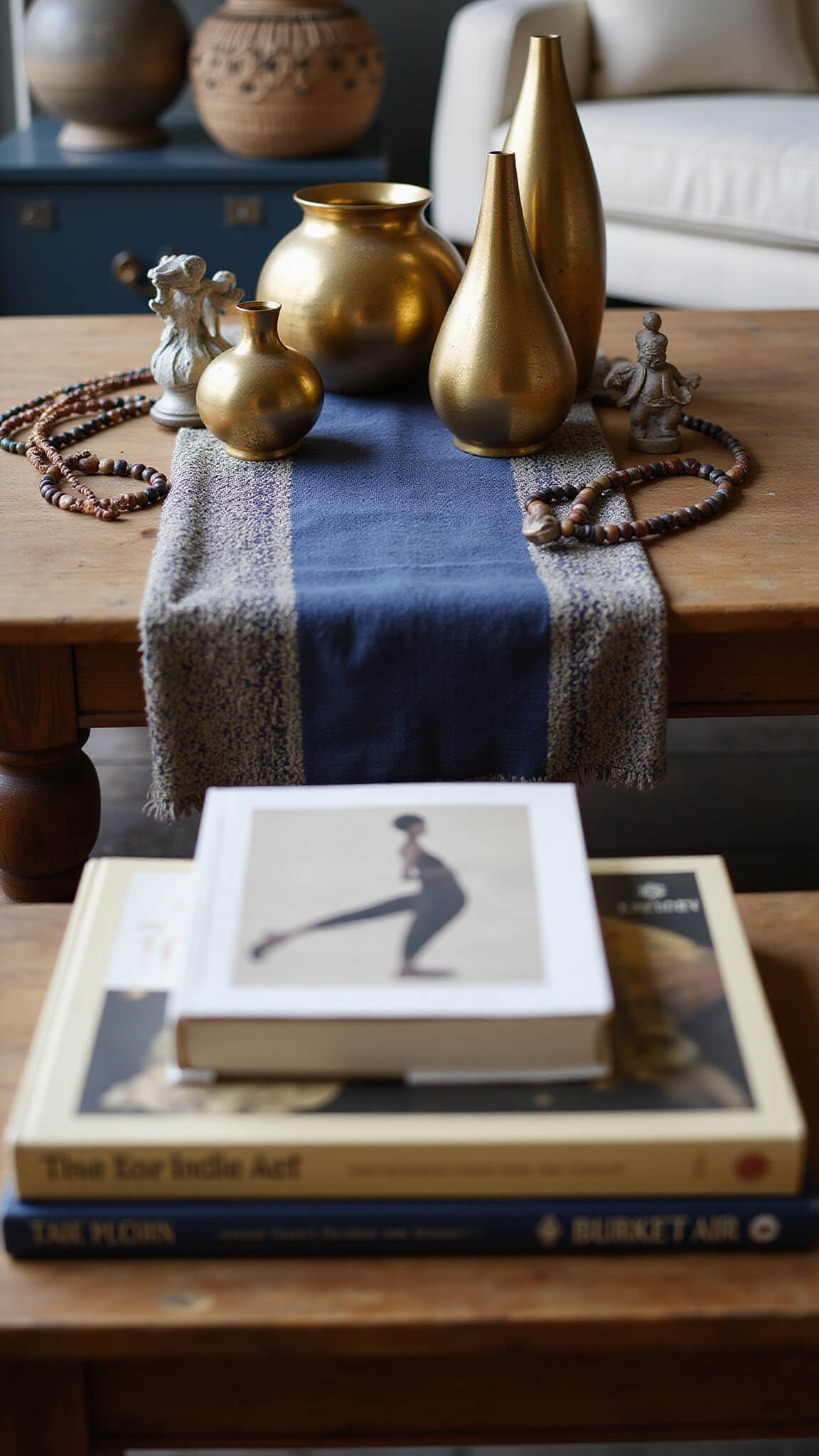 Close-up of a styled wooden coffee table with ceramic vessels, brass figurines, beaded decor, and African art books, lit by soft natural morning light.