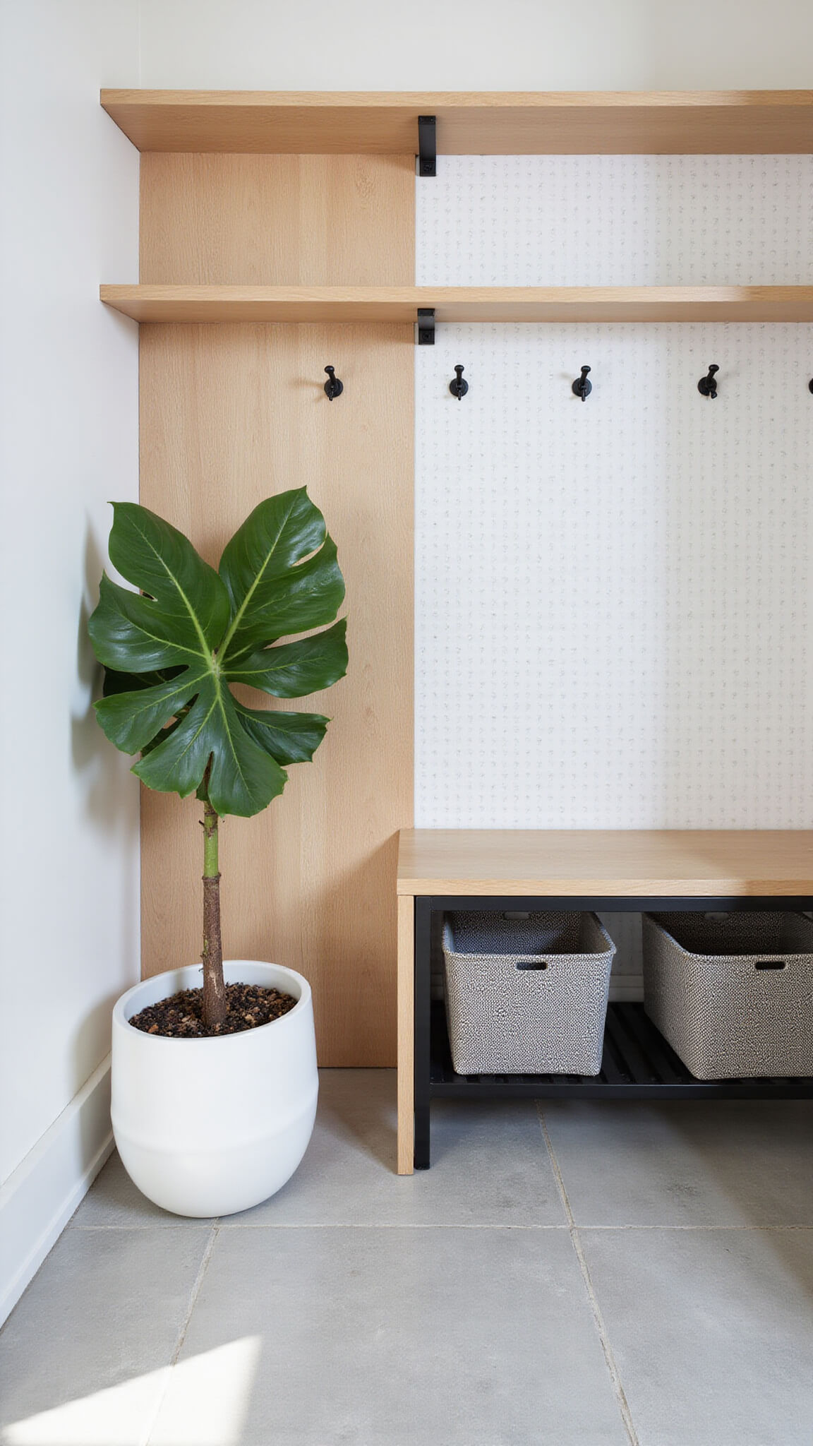 Modern Scandinavian entry hall with white oak pegboard wall, black metal console, monstera plant, and light gray limestone floor.
