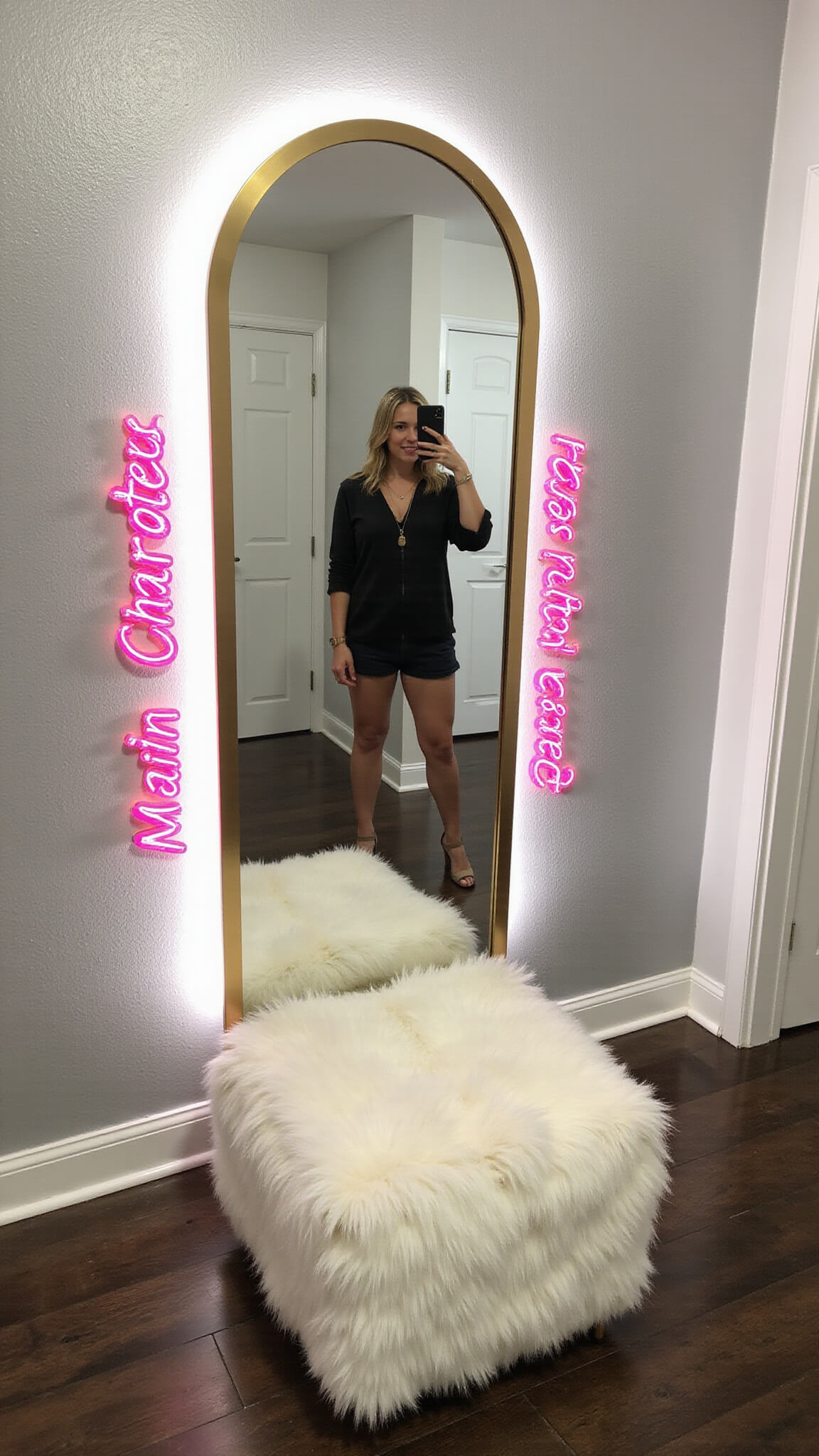 Late afternoon selfie wall with large arched mirror, gold frame, neon pink 'Main Character Energy' sign, silver metallic wallpaper, LED halo lighting, and white faux fur ottoman.