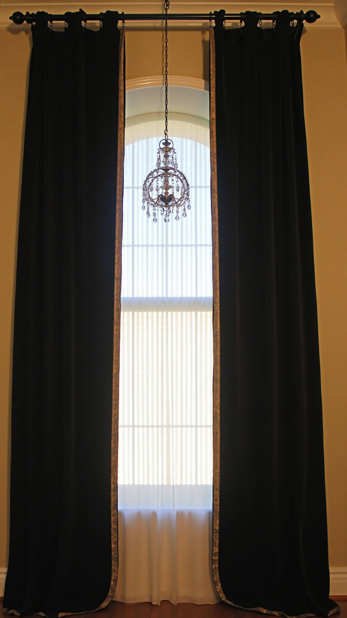 Golden hour view of tall window wall with black velvet drapes, metallic trim, crystal chandelier, and prismatic light effects.