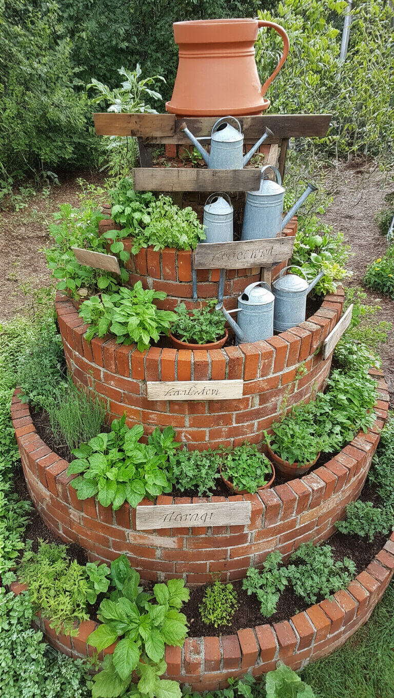Eye-level view of a 10-foot herb spiral made from reclaimed brick with vintage zinc edging, featuring terracotta pots, old watering cans, and weathered wooden herb markers among lush green herbs.
