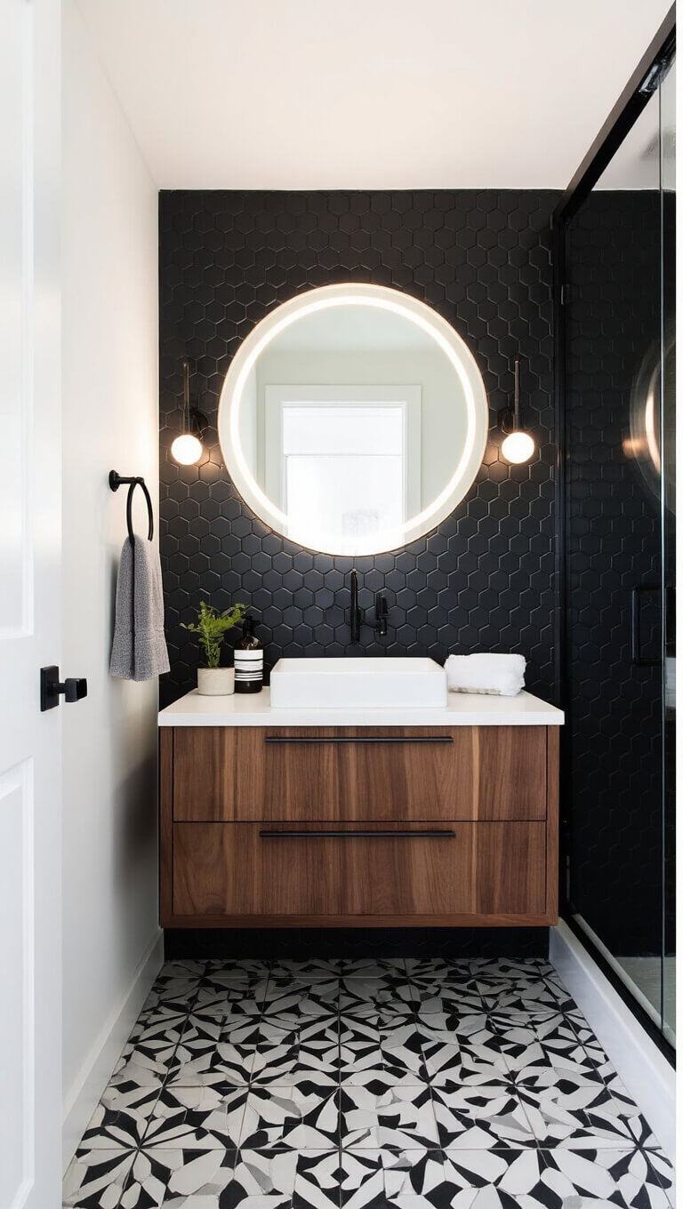Modern small bathroom with black hexagonal wall tiles, white fixtures, walnut floating cabinet, round LED mirror, and matte black accents.