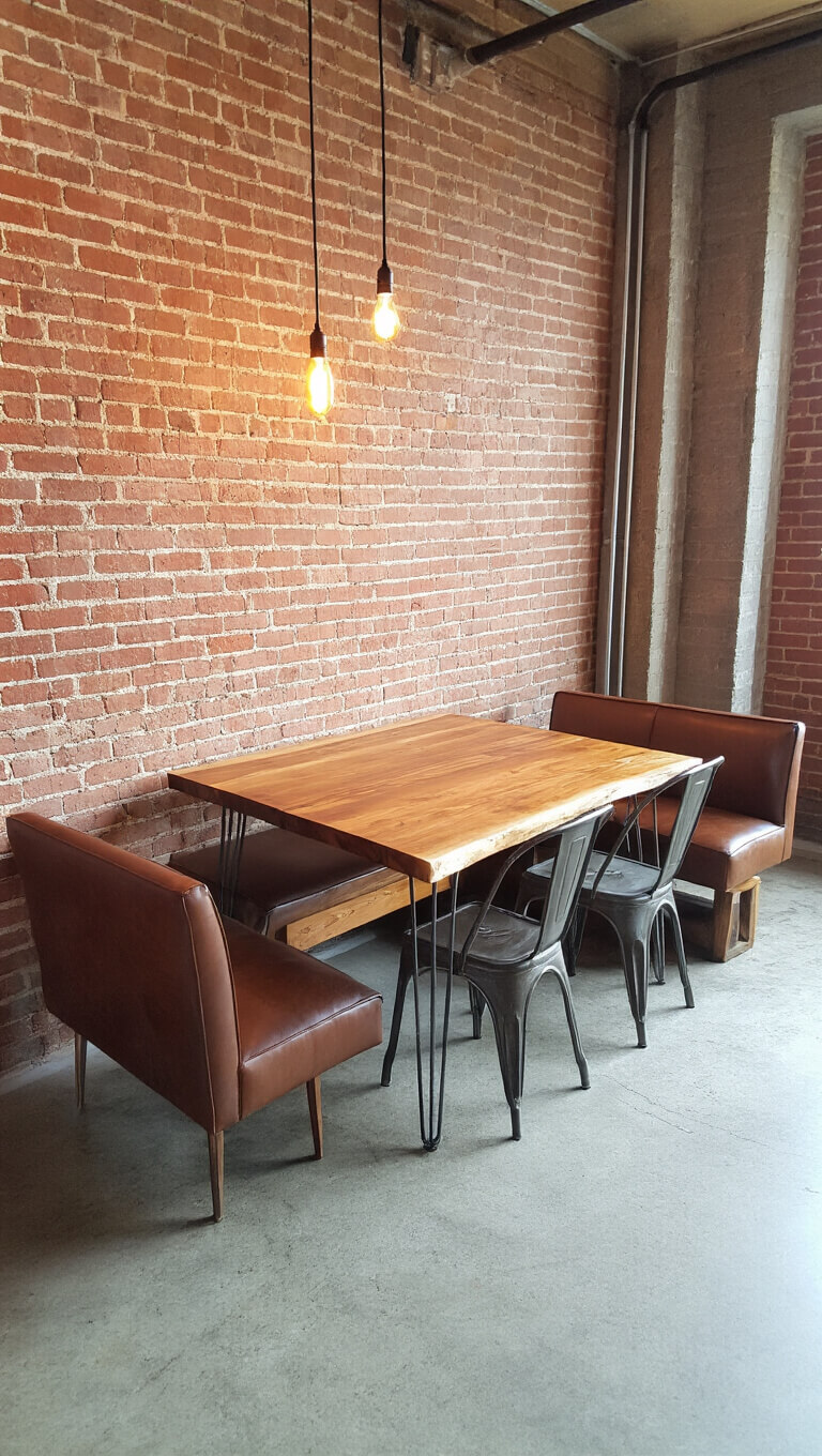 Compact urban industrial corner with exposed brick, wall-mounted wood table, mixed seating, and Edison bulb lighting.