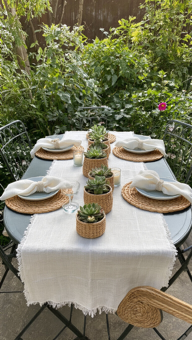 Midday garden party with earth-toned table setting, featuring layered textiles, potted succulents, and tealights on a 4ft bistro table.